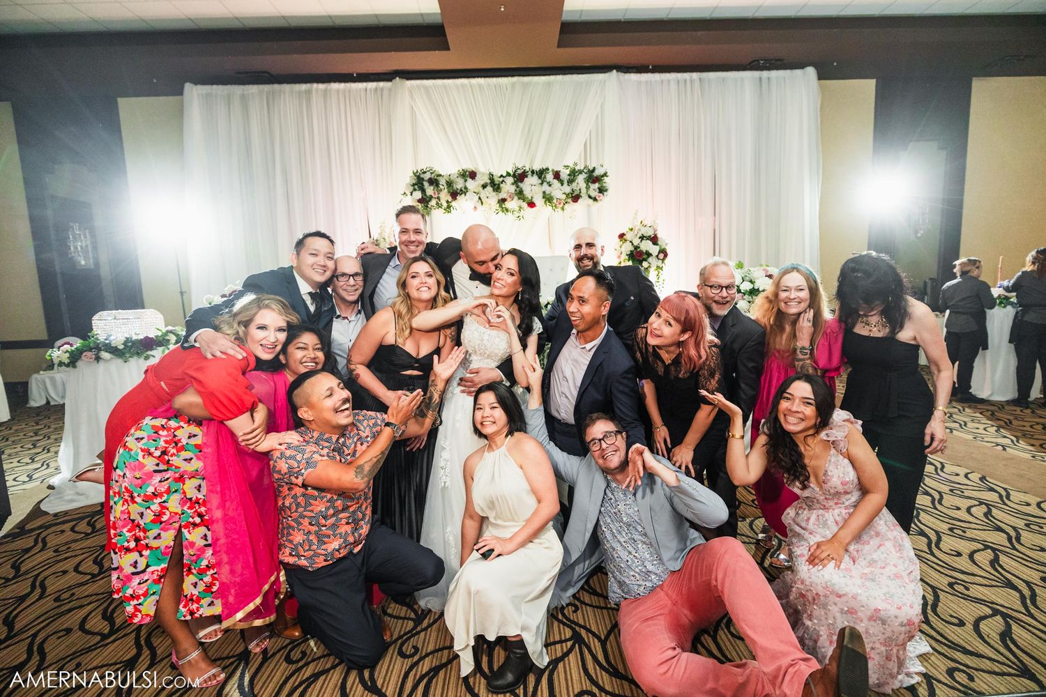 Wedding guests gather for a fun group photo with the newlyweds in a reception hall.