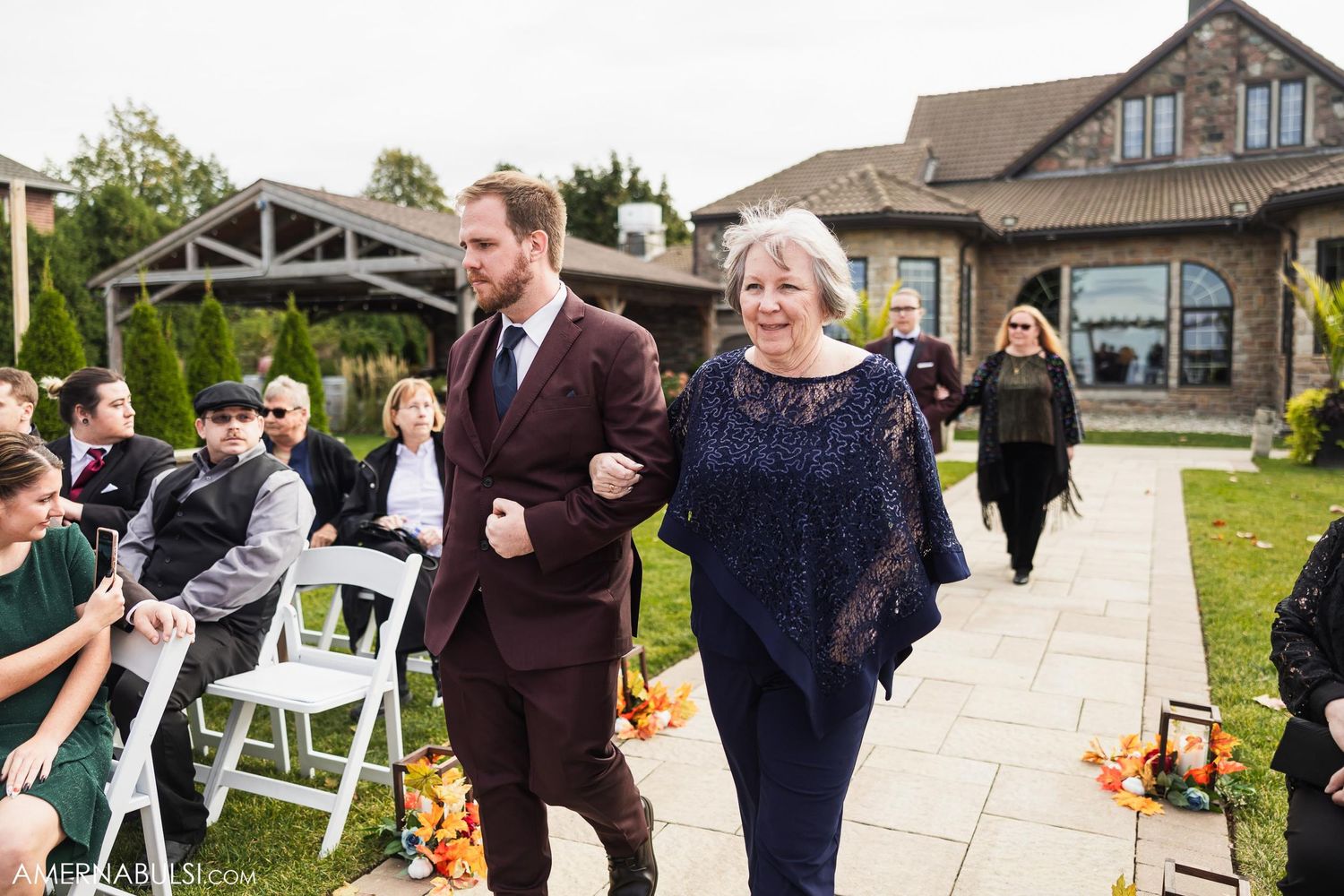 Wedding ceremony procession walking down stone pathway past seated guests.