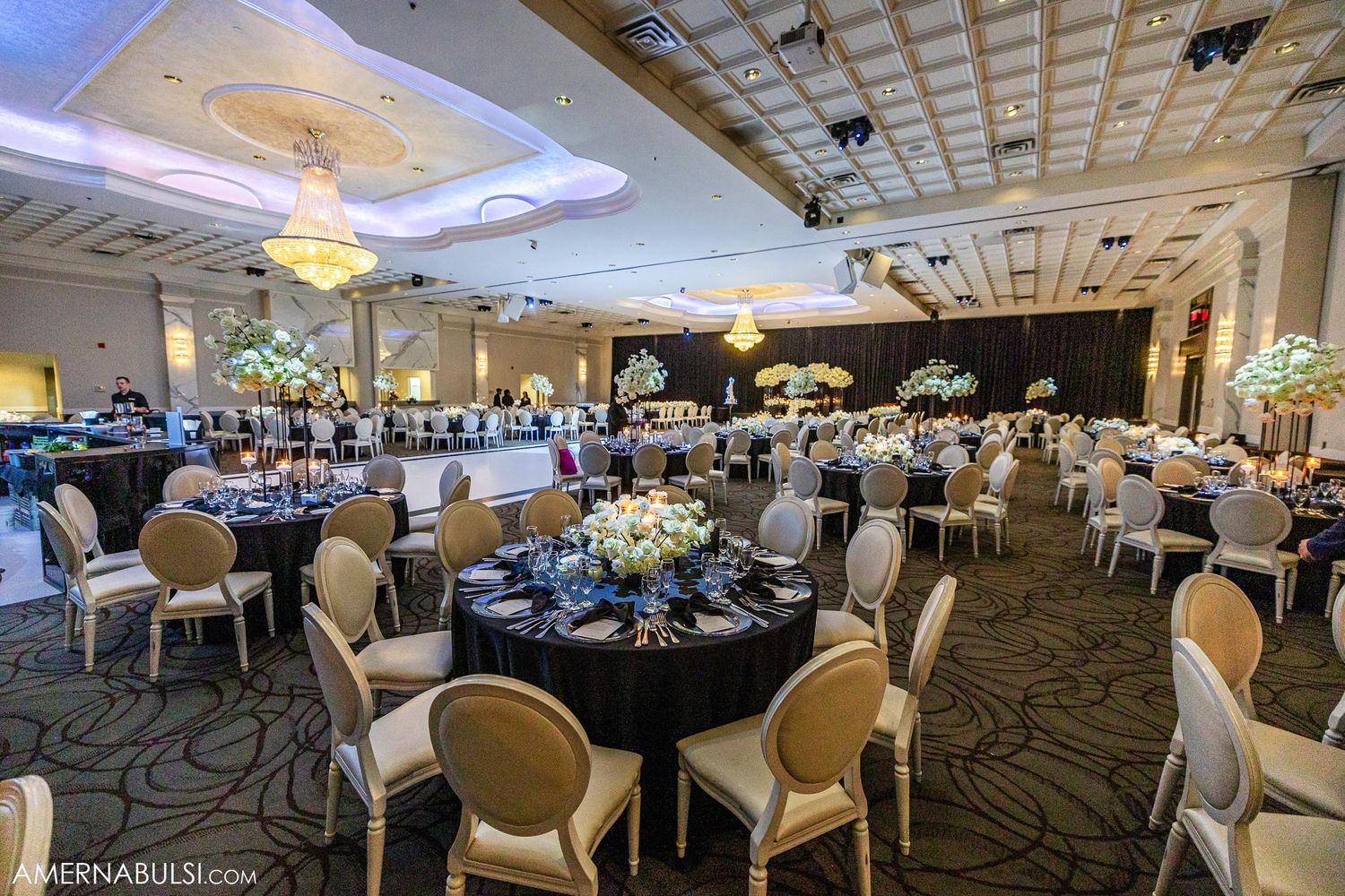 Elegant ballroom setup with round tables, cream chairs, and floral centerpieces for wedding reception.