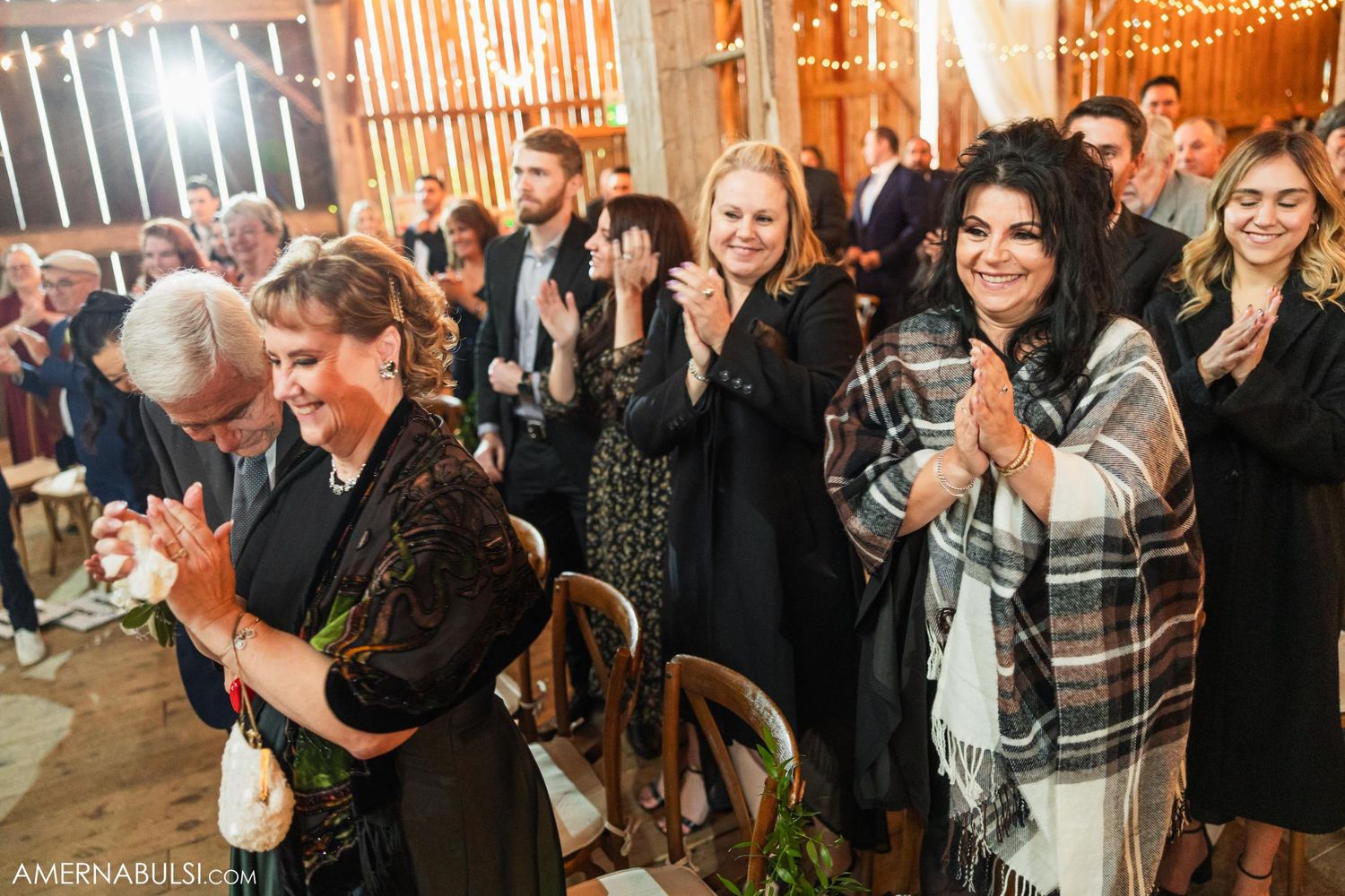Wedding guests applaud and celebrate in rustic barn reception venue.