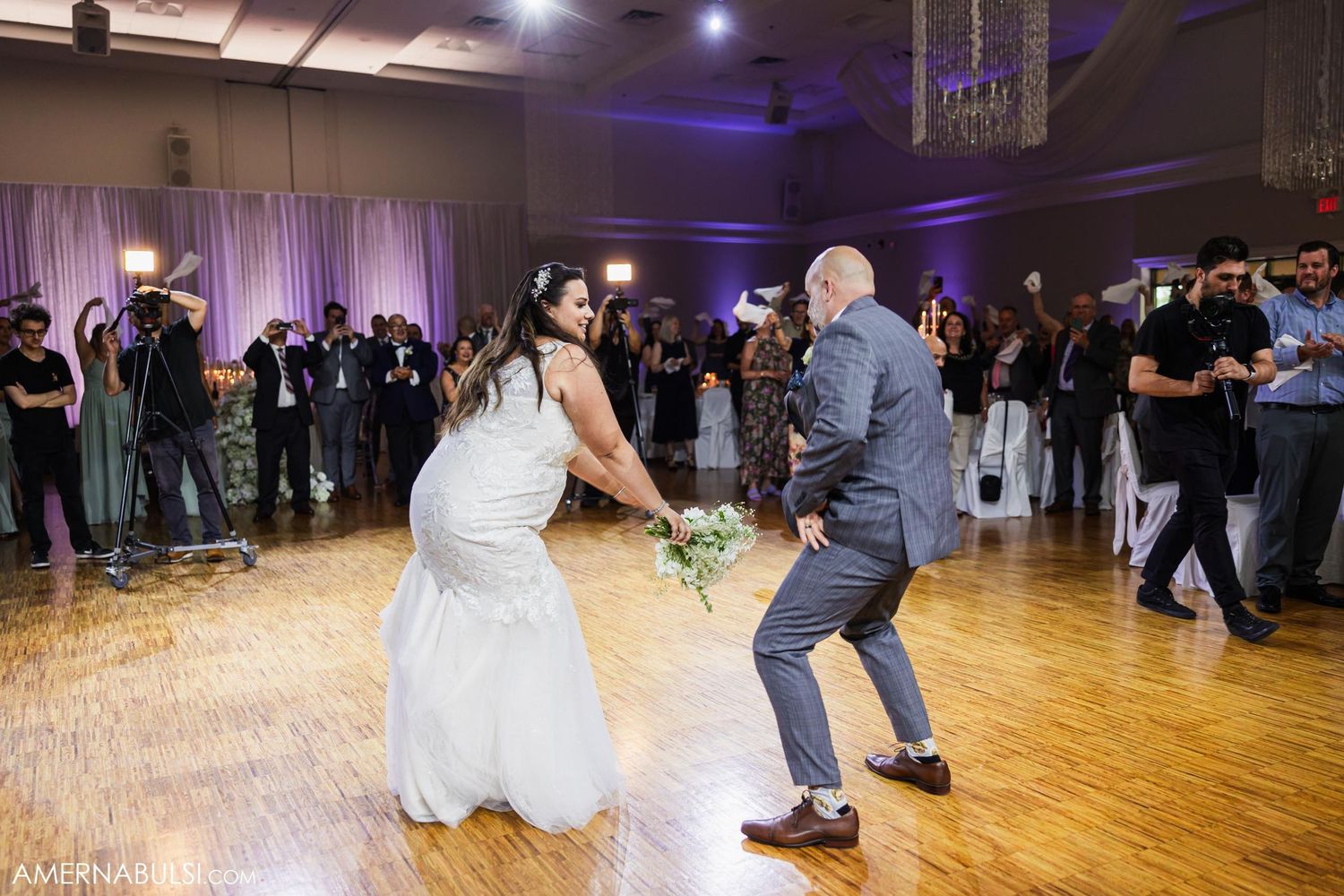 Energetic dance moves on wooden floor during wedding reception with purple accent lighting.