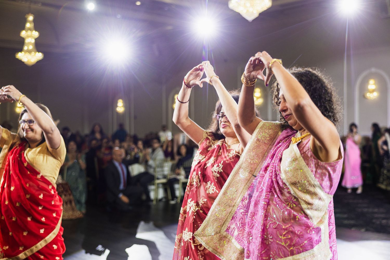 Dancers in vibrant traditional Indian outfits performing choreographed moves at an indoor event.