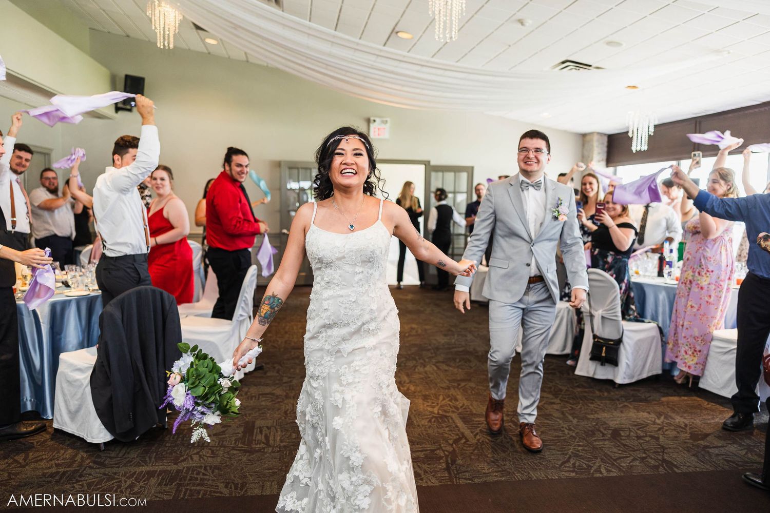 Newlyweds make their entrance into a reception hall decorated with white ceiling drapes.