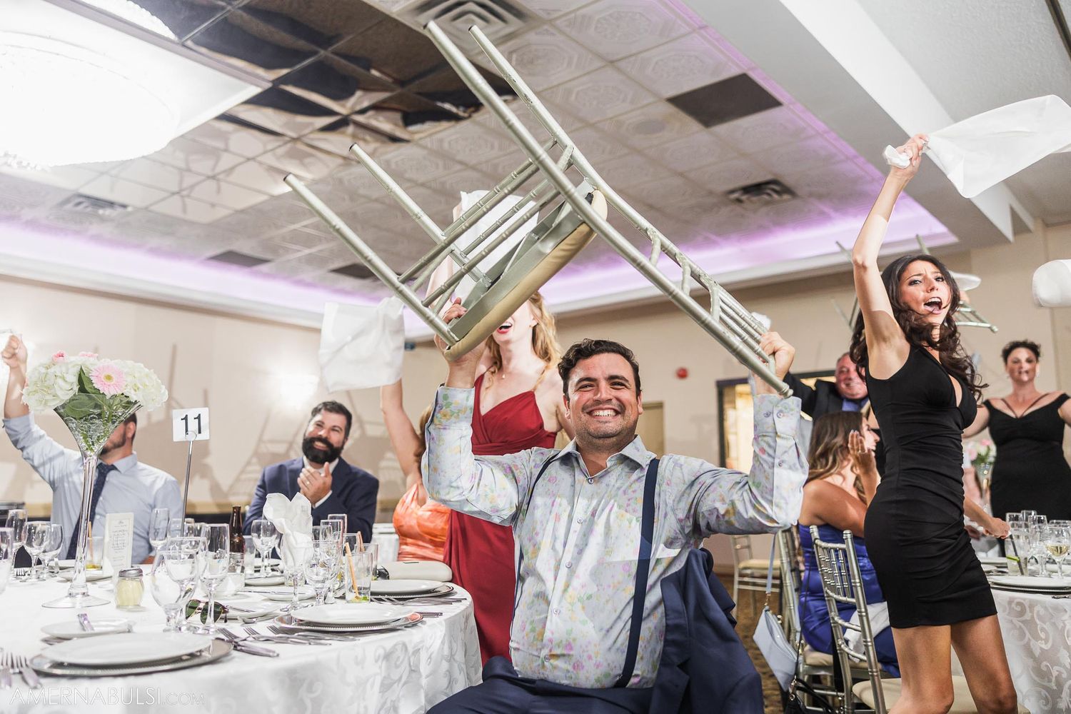 Wedding reception guests raise glasses in celebratory toast at decorated banquet table.