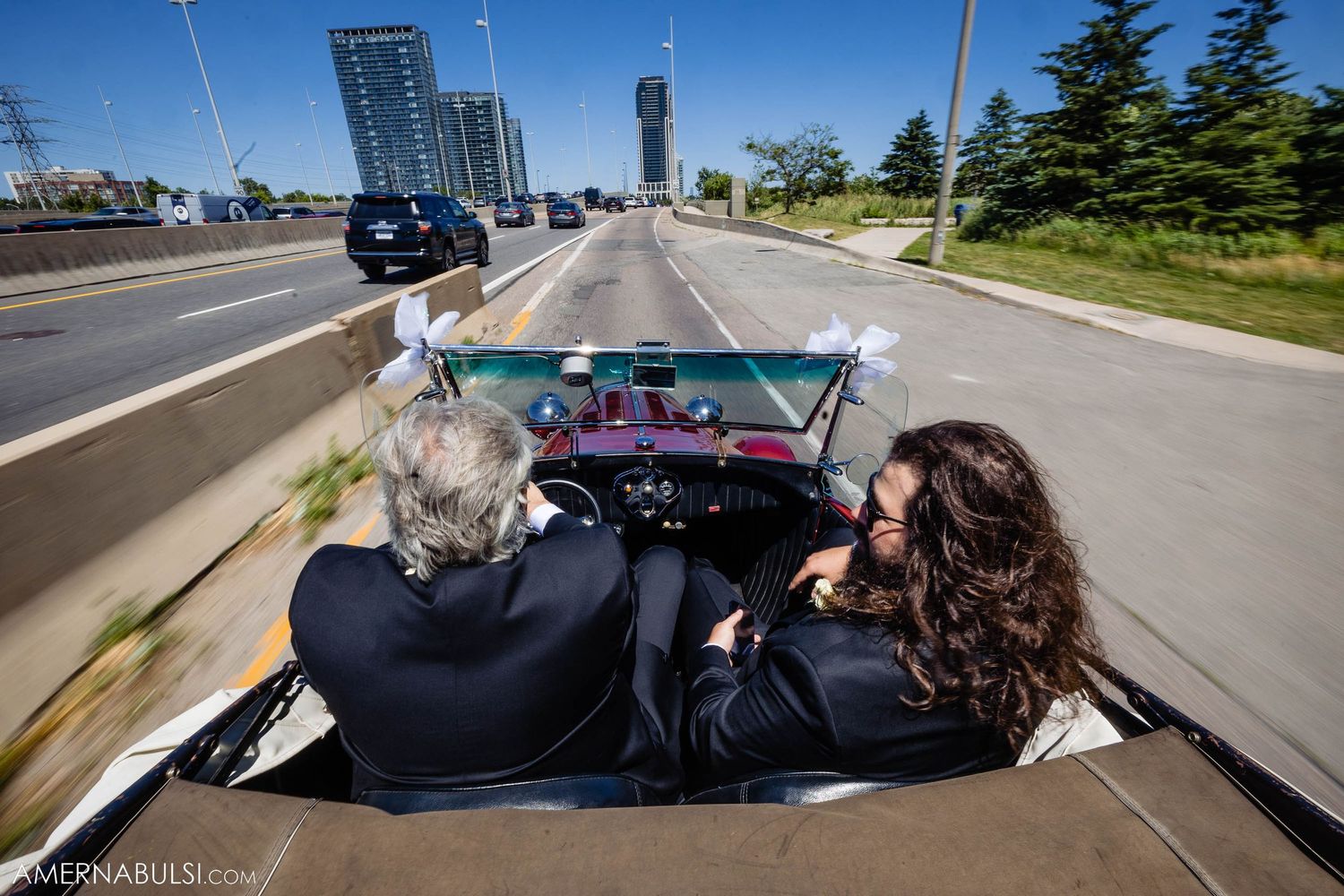Two people ride in vintage convertible car through city streets.