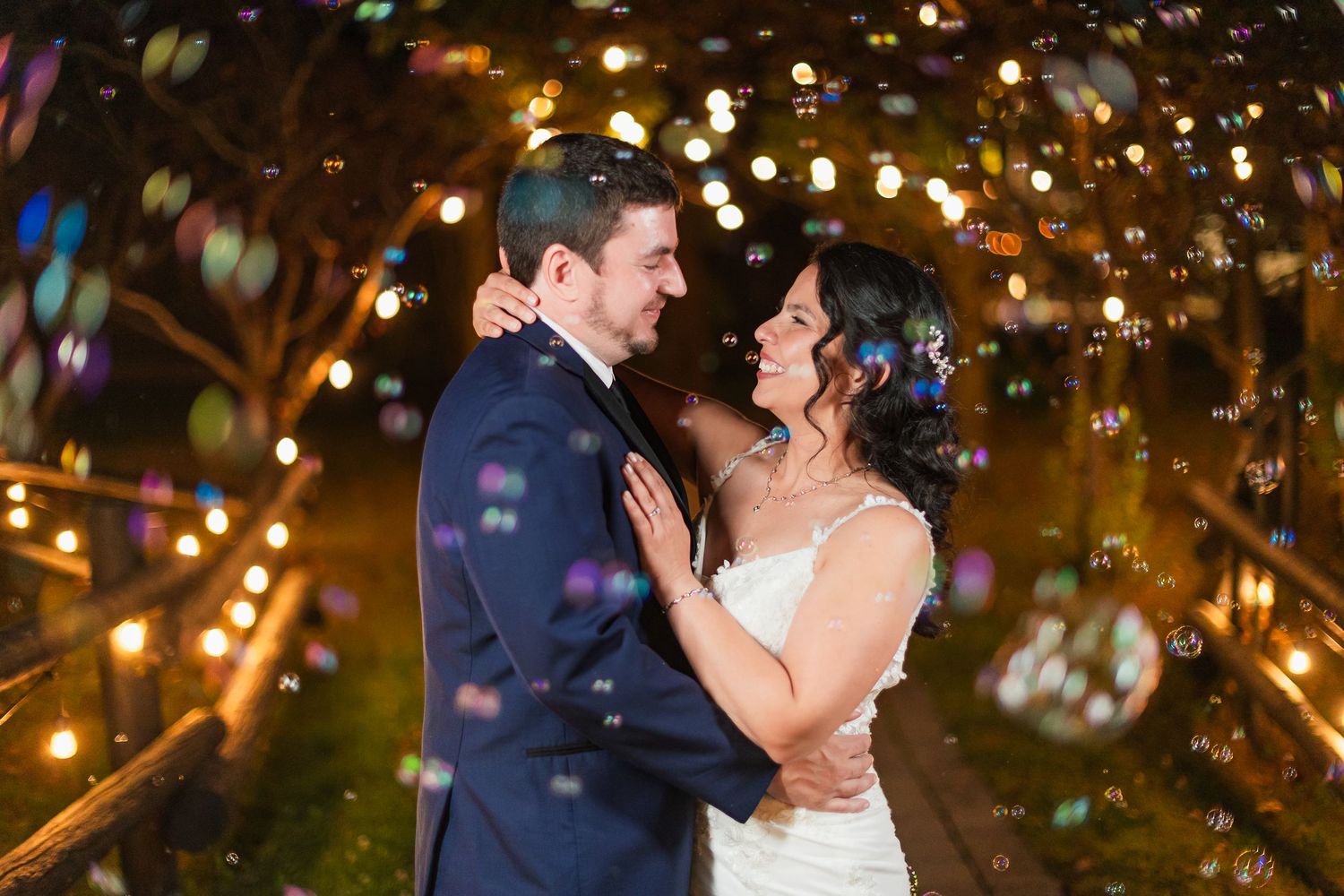 Newlyweds share a romantic moment surrounded by bubbles and bokeh lights at their wedding.