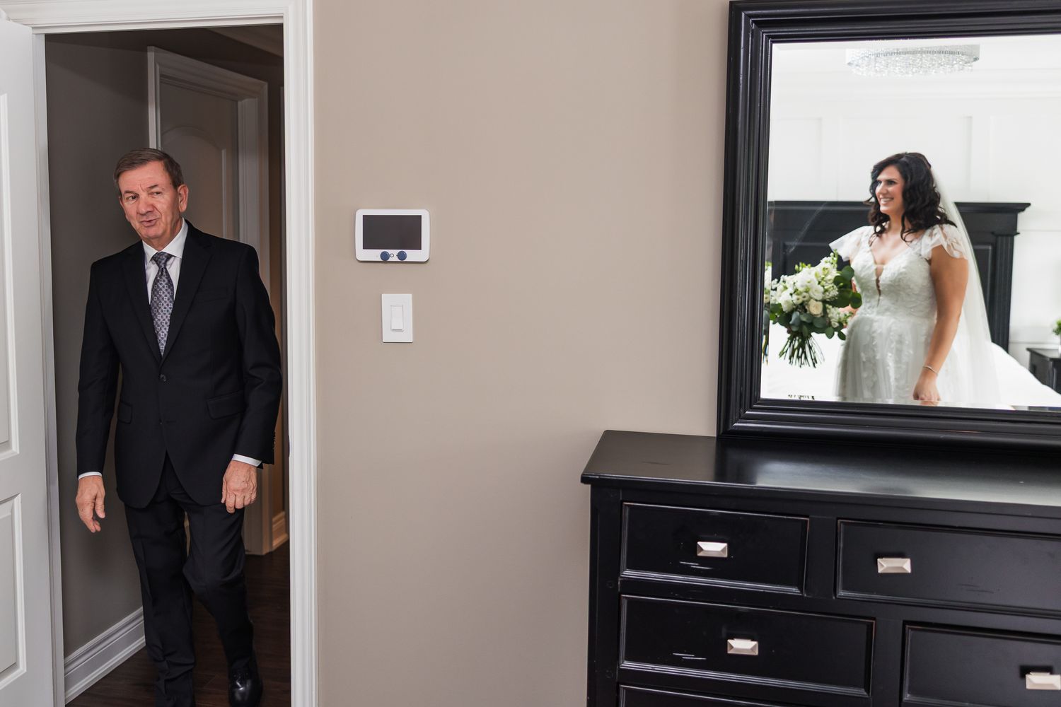 Father of the bride entering room seeing bride's reflection in mirror wearing white wedding gown.