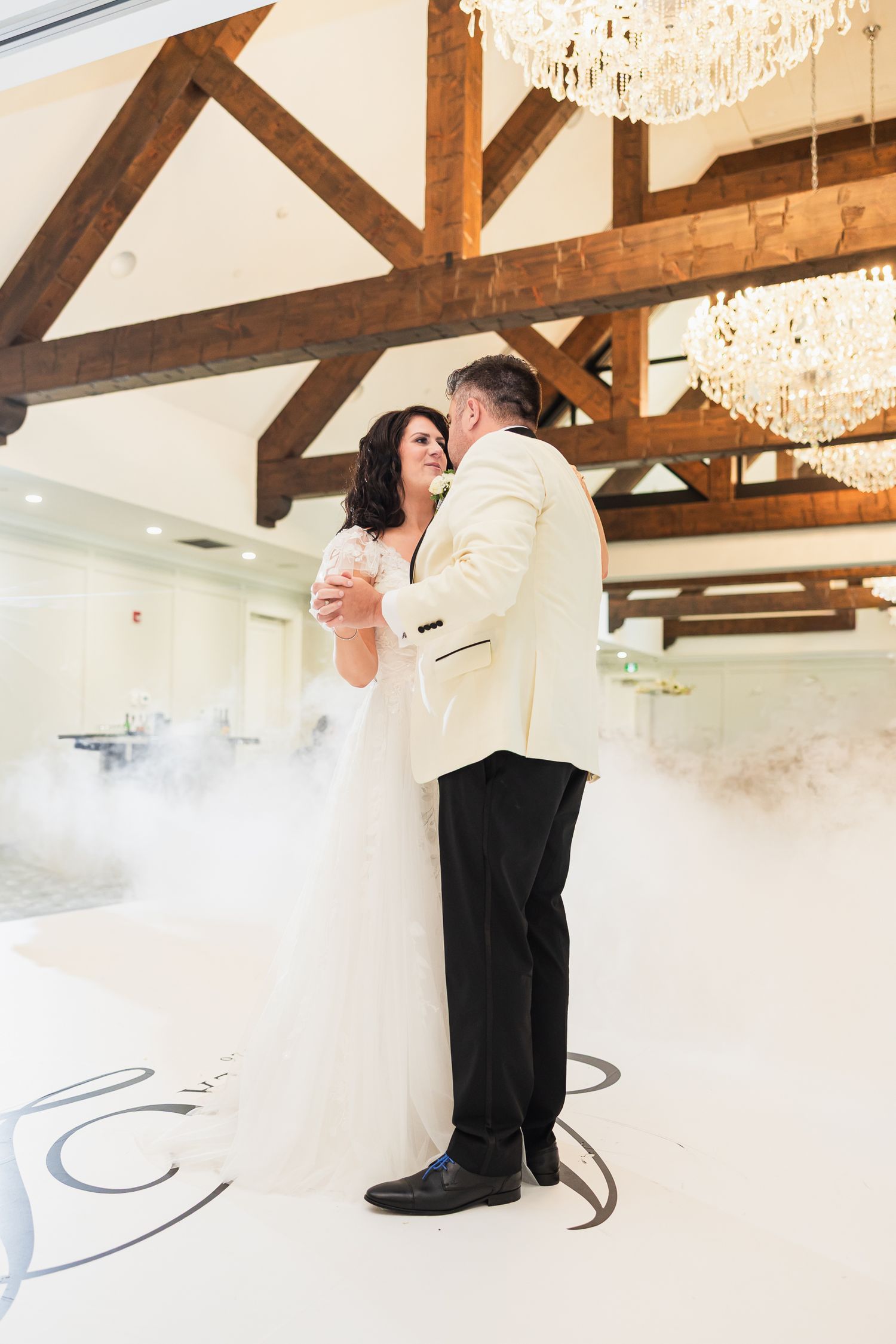 Bride and groom share their first dance on a white dance floor surrounded by romantic fog in an elegant venue.