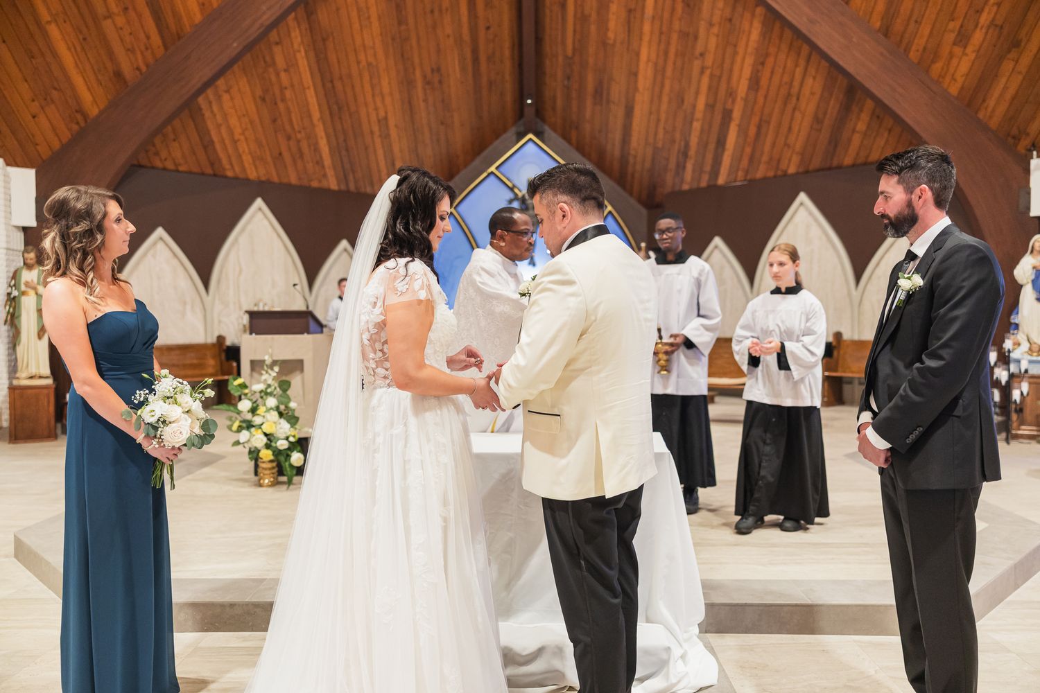 Bride and groom exchange vows at church altar with bridesmaid and groomsman standing nearby during wedding ceremony.