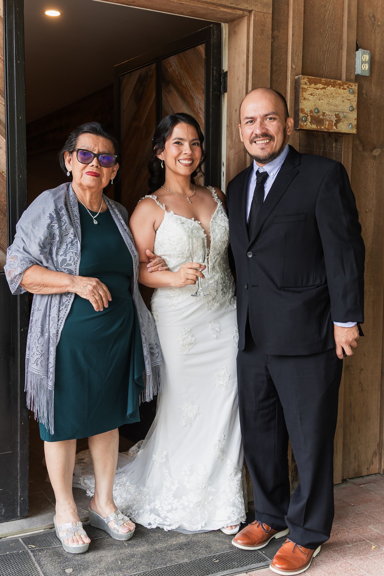 Bride in lace gown posing with family members at rustic barn wedding venue.