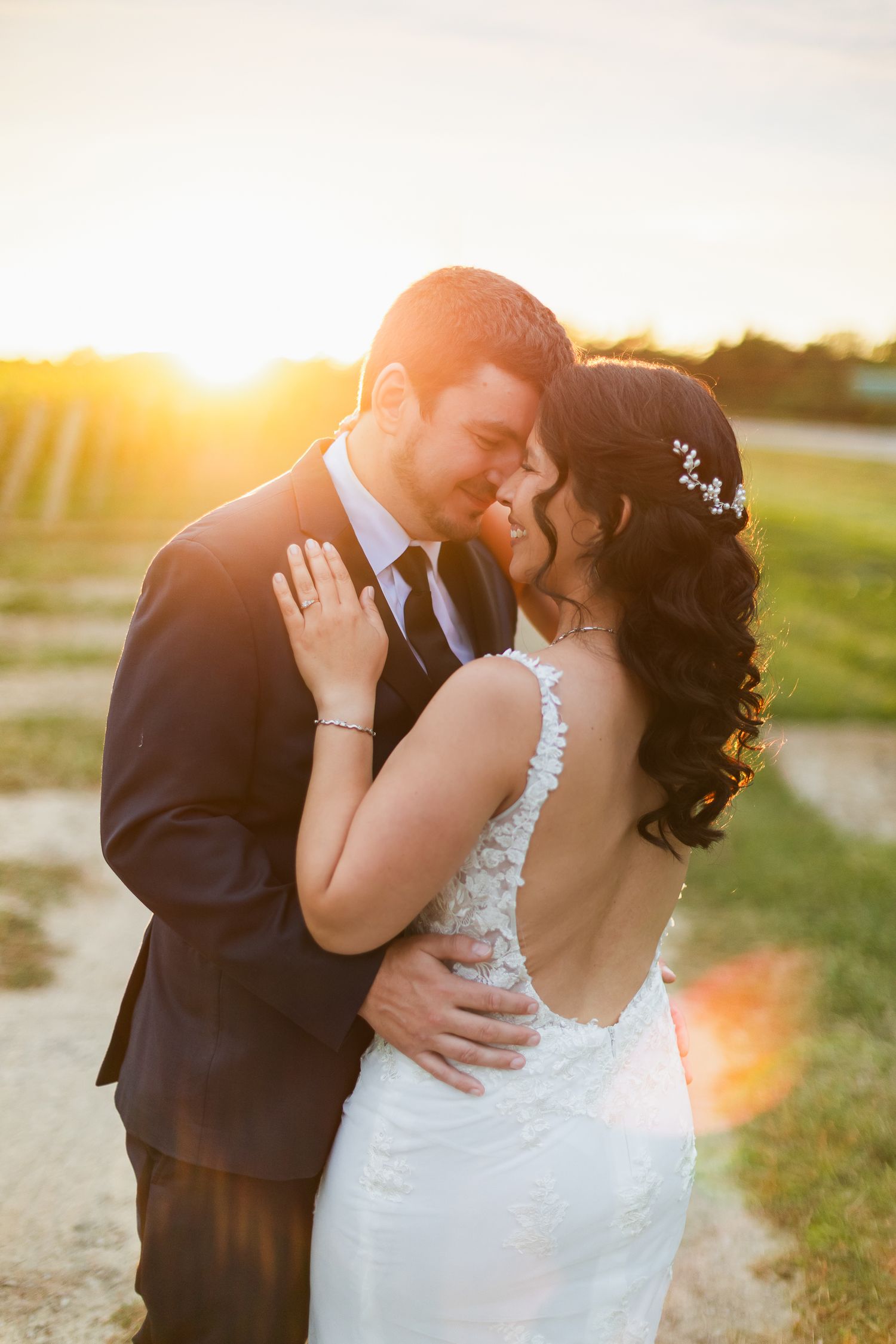 Bride and groom share a romantic sunset embrace outdoors, golden hour light glowing behind them on their wedding day.