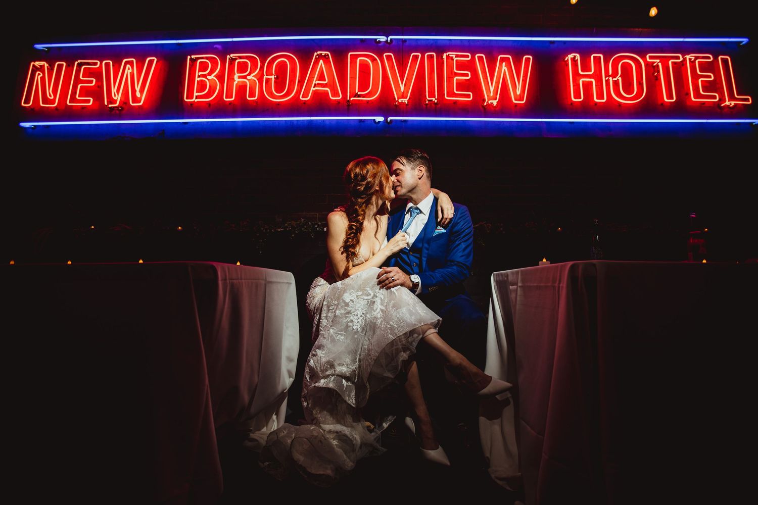 Wedding couple silhouetted against red neon New Broadview Hotel sign at night.