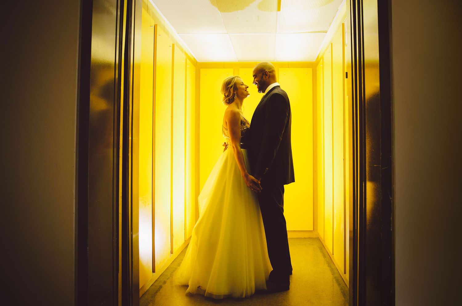 Artistic wedding portraits in yellow-lit hallway creating dramatic silhouettes and shadows.