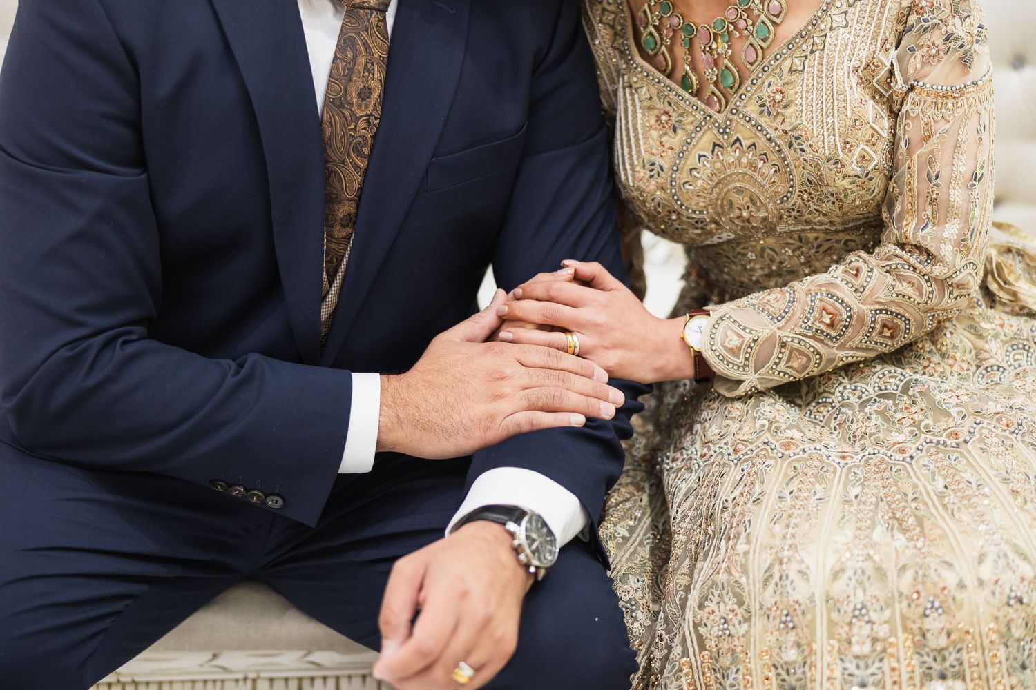 Close-up of couple's hands clasped together showing formal attire and jewelry.