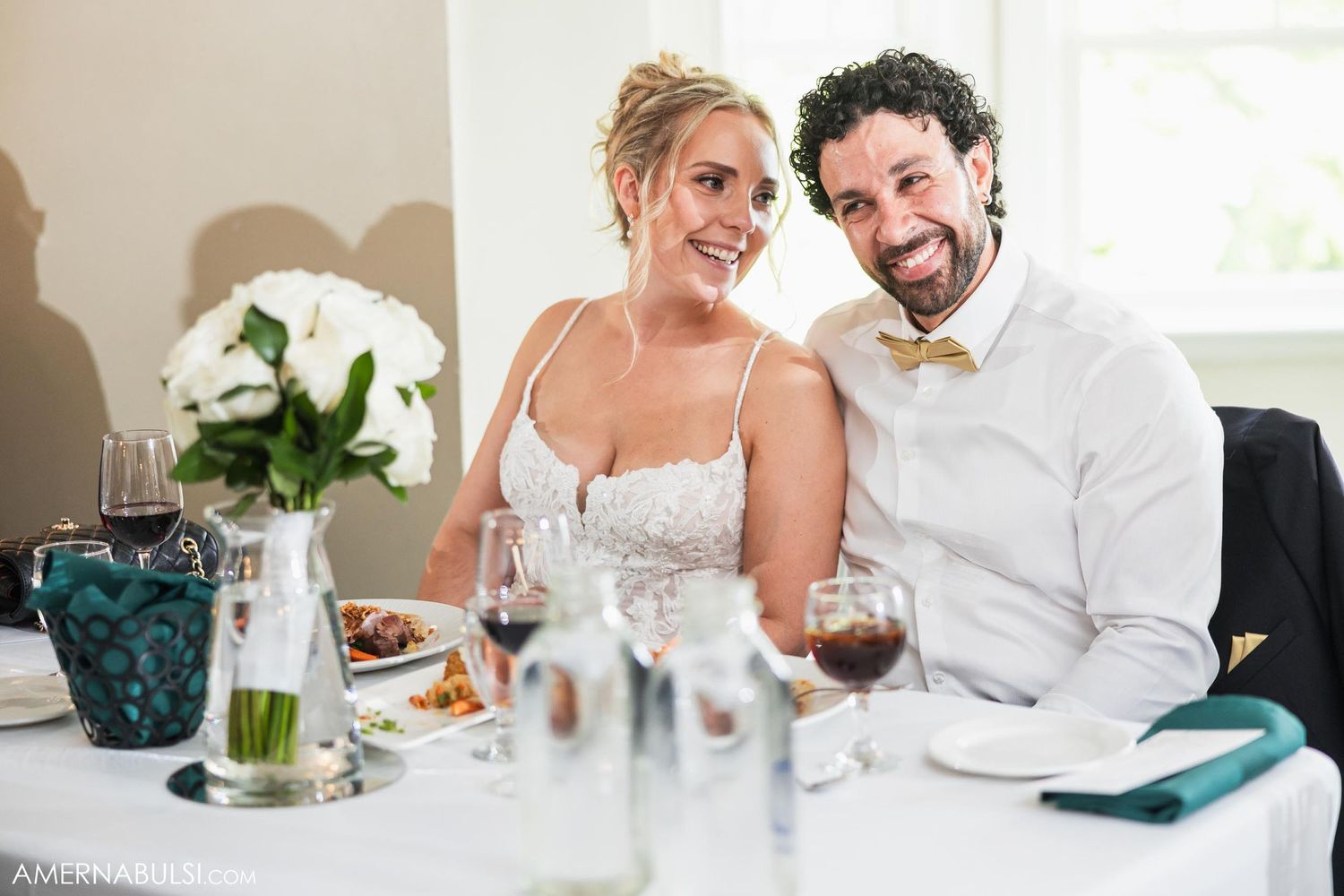 Couple sharing a candid moment at their reception table with wine glasses and floral decor.
