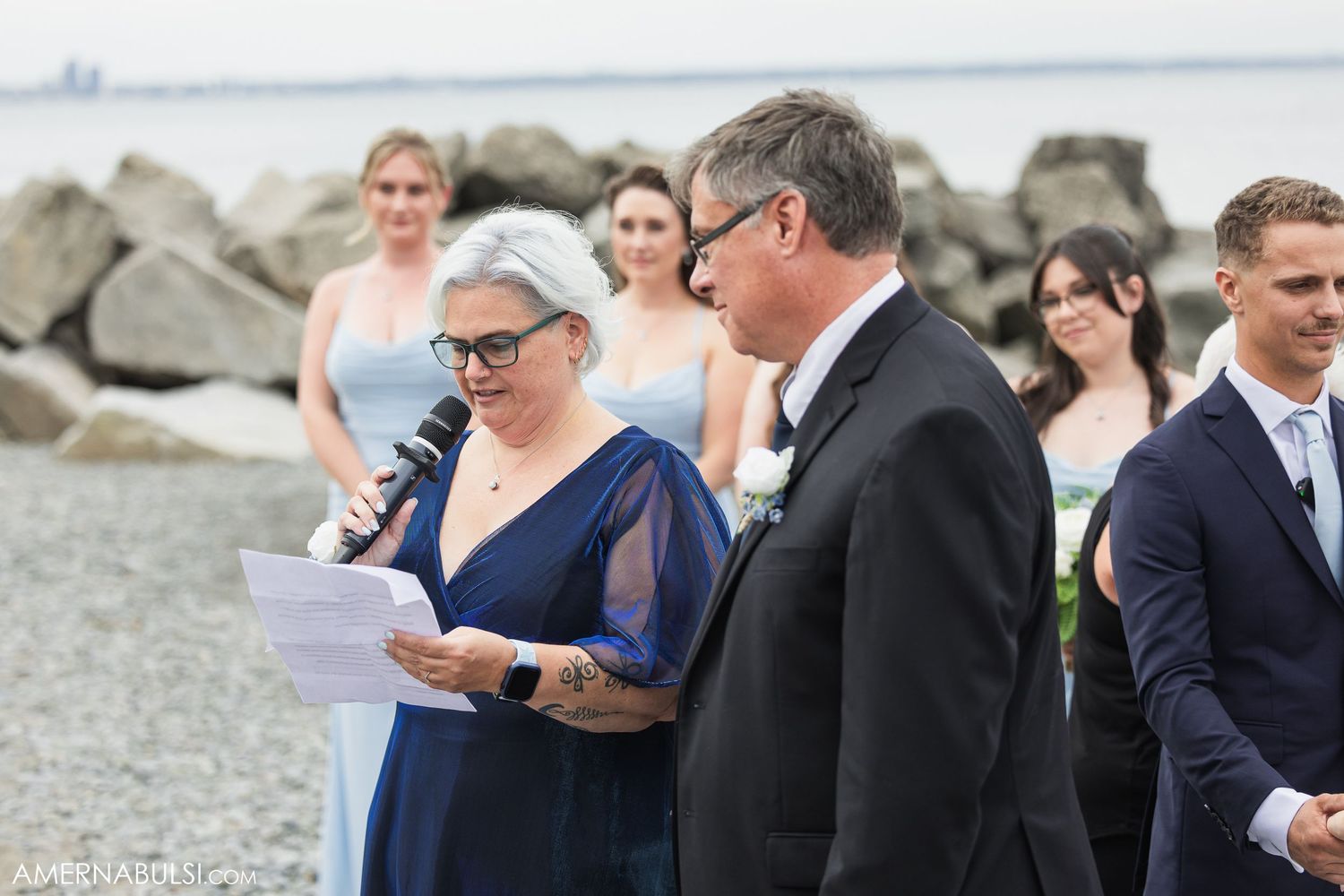 Wedding attendees gather near a rocky shoreline during an outdoor ceremony.