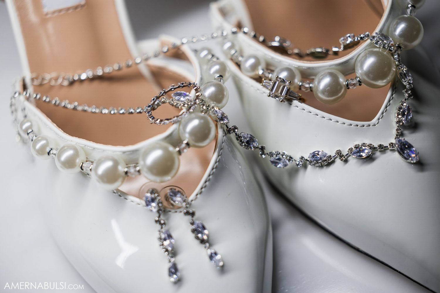 Close-up detail of elegant white bridal shoes adorned with pearl and crystal embellishments on a delicate chain.