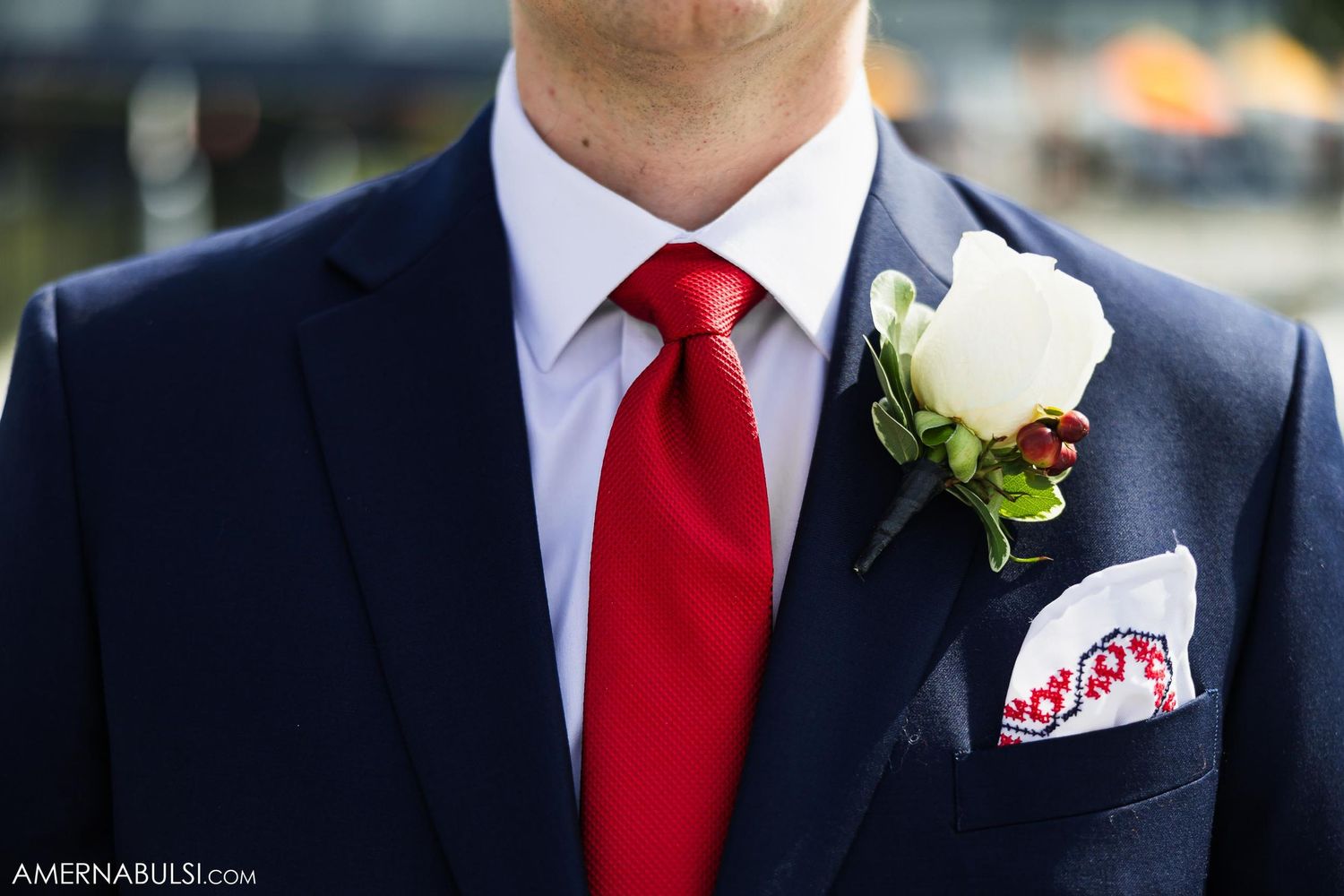 A closeup of a groom's navy suit with red tie and white rose boutonniere.