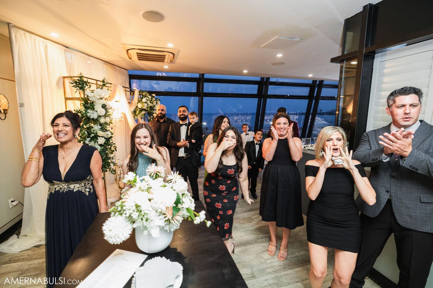Wedding guests react with surprised expressions during a celebration in an elegant indoor venue.