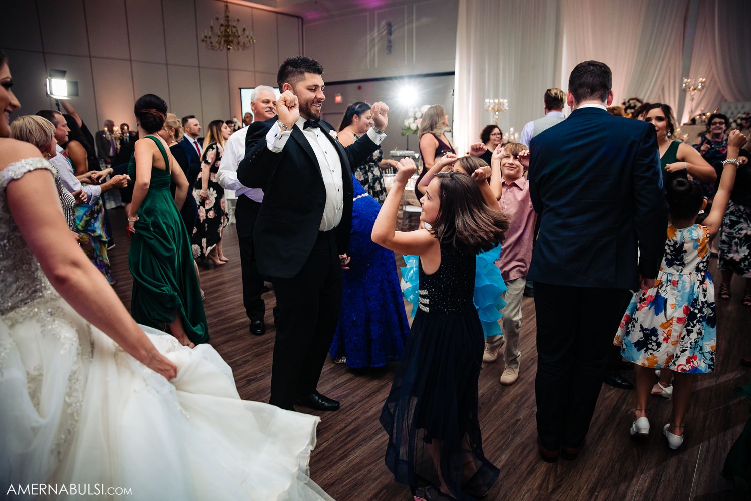 Wedding guests dancing together on a crowded reception dance floor with colorful lighting and festive atmosphere.