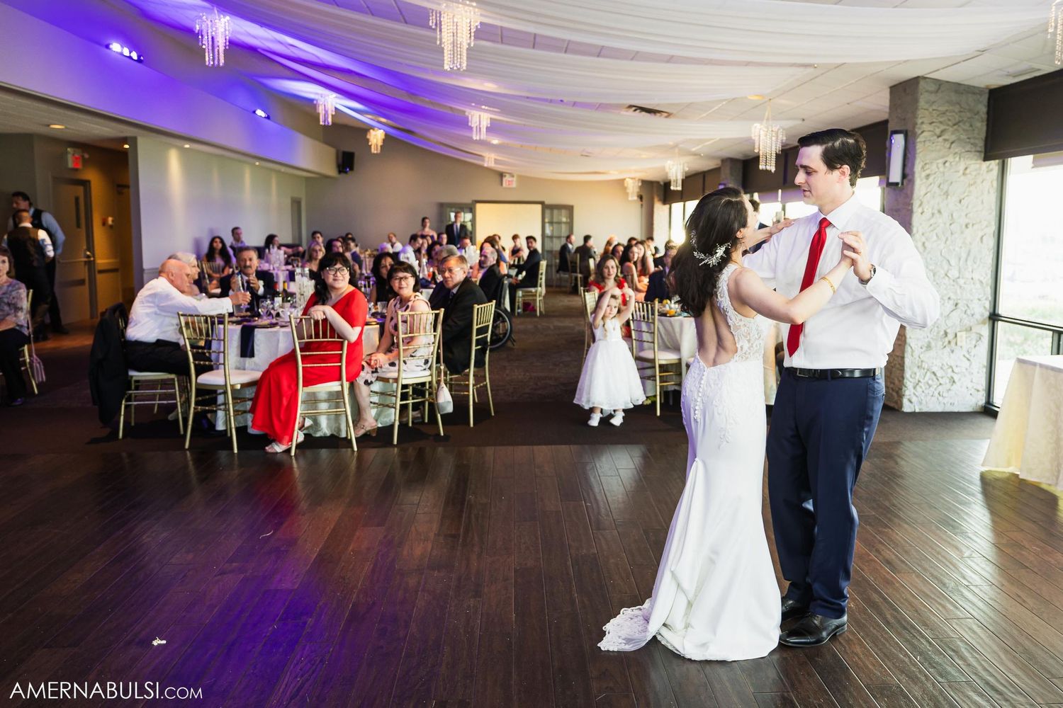 Wedding reception dance floor scene with guests seated at decorated tables.