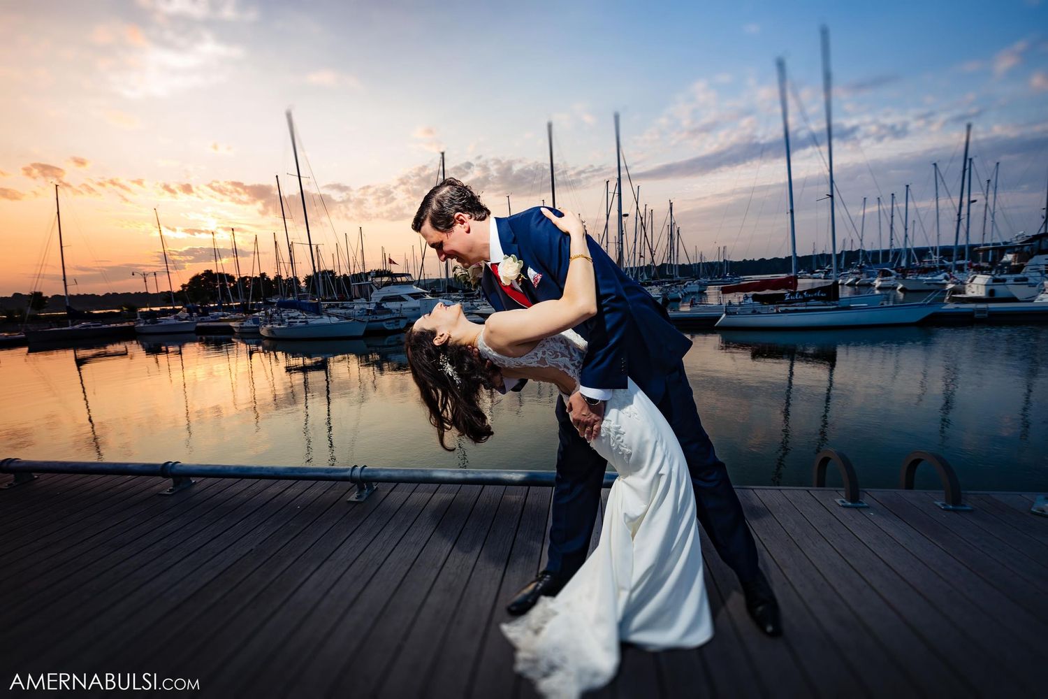 Dramatic dip pose on marina dock during sunset with sailboats in background.