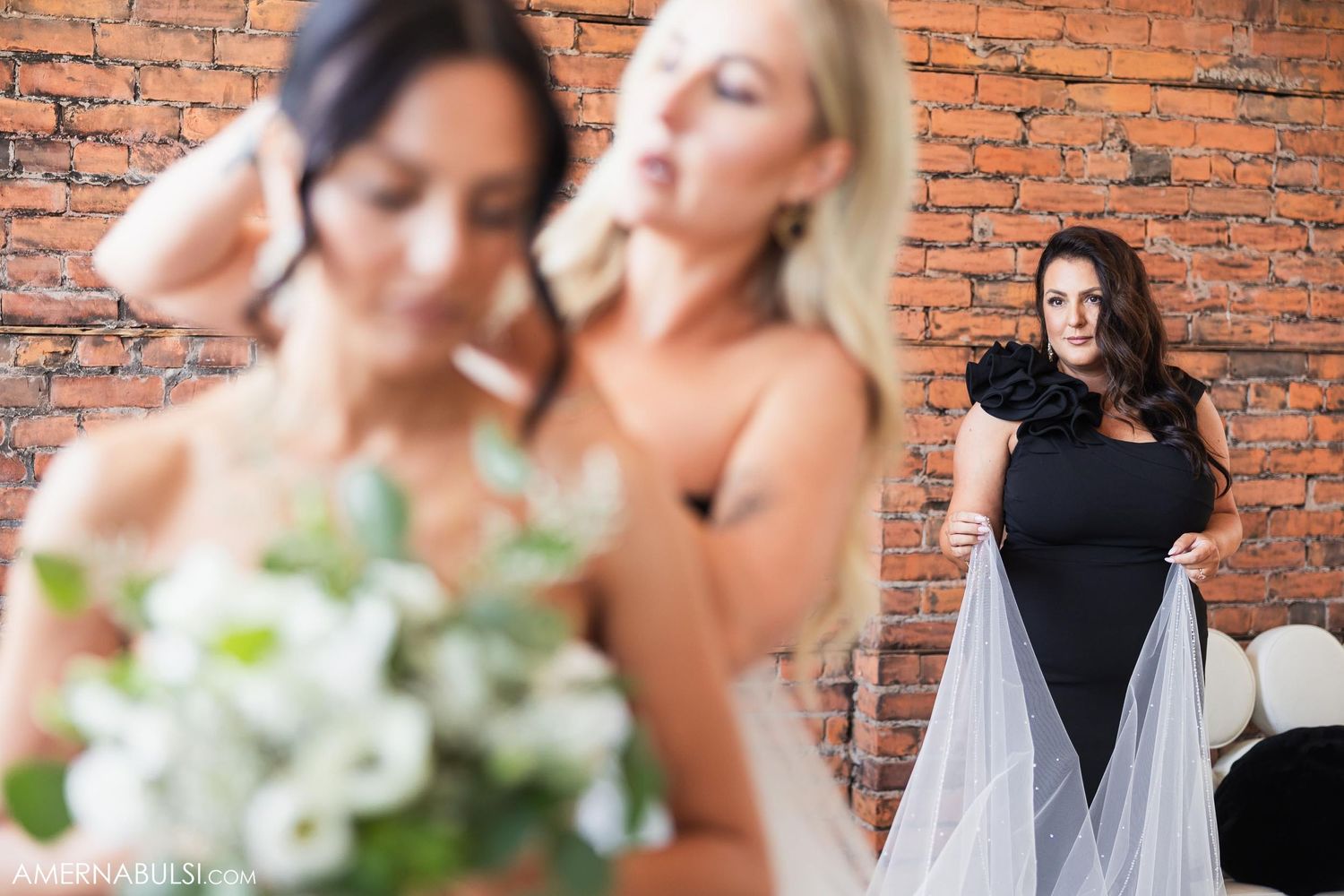 Wedding party members interact during bridal preparation in front of brick walls.
