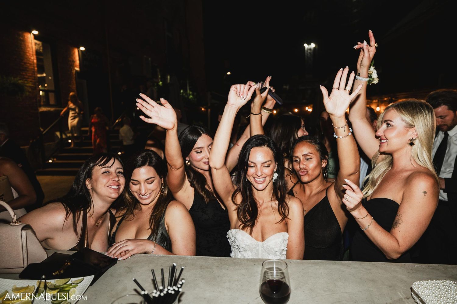 Group of friends celebrating with raised hands at reception dinner table.