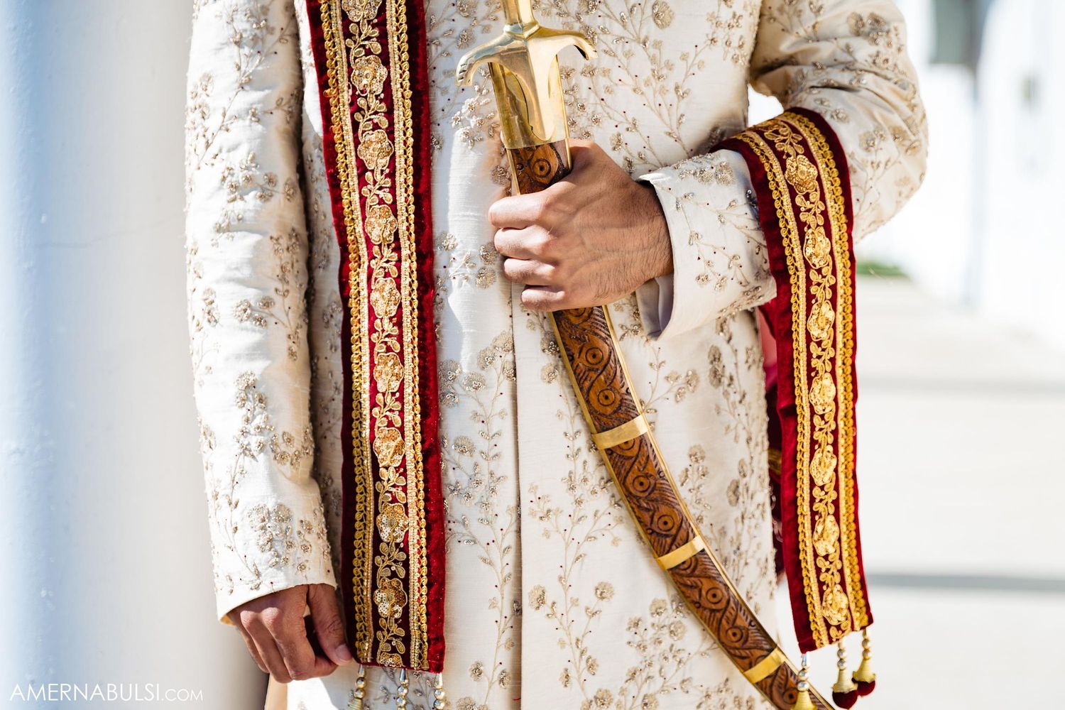 Close-up of traditional Indian groom's sherwani with gold embroidery and ceremonial sword.