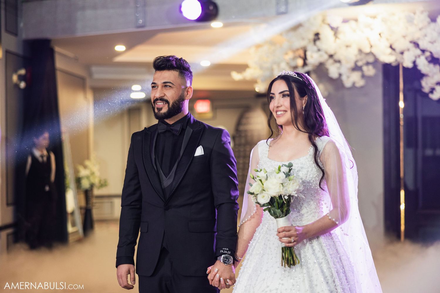 Elegant wedding reception scene with romantic lighting, white floral arrangements and dancing couples on the dance floor.