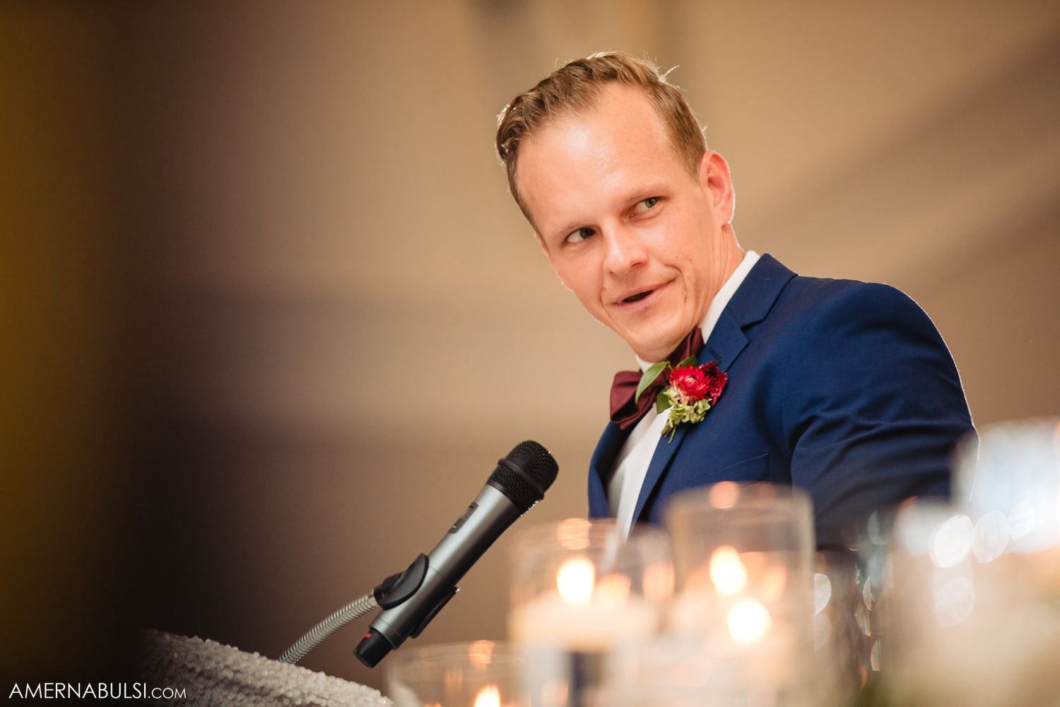 A person in a navy suit speaks into a microphone during a formal event.