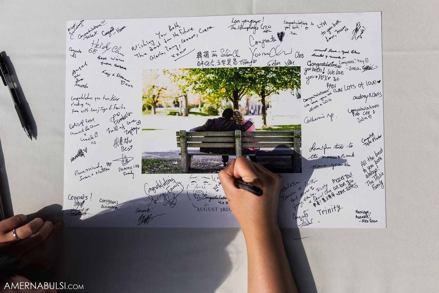 Guest signing a photo guestbook with handwritten messages surrounding a bench picture.