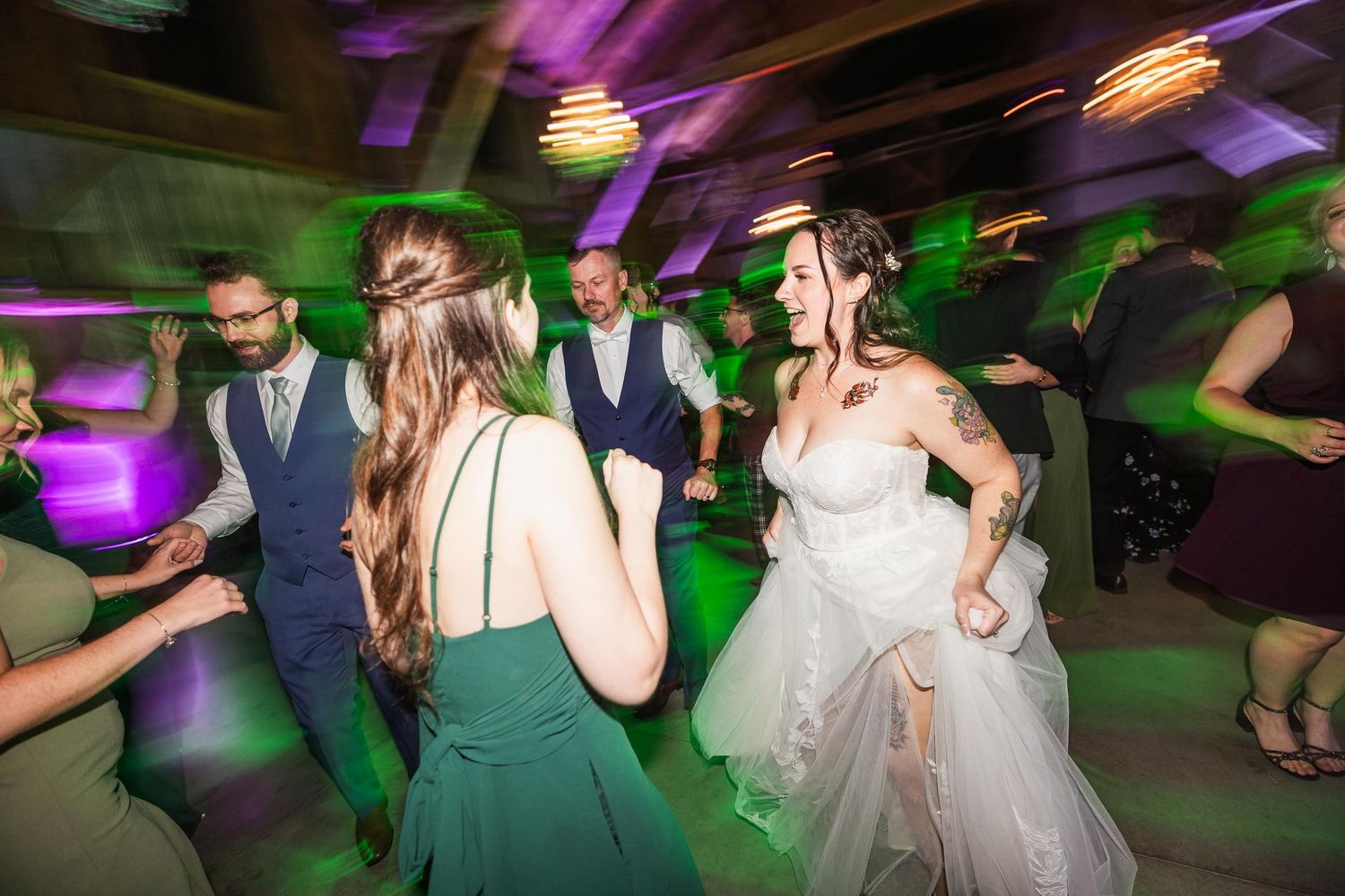 Wedding guests dancing at reception with colorful disco lighting and motion blur effects.