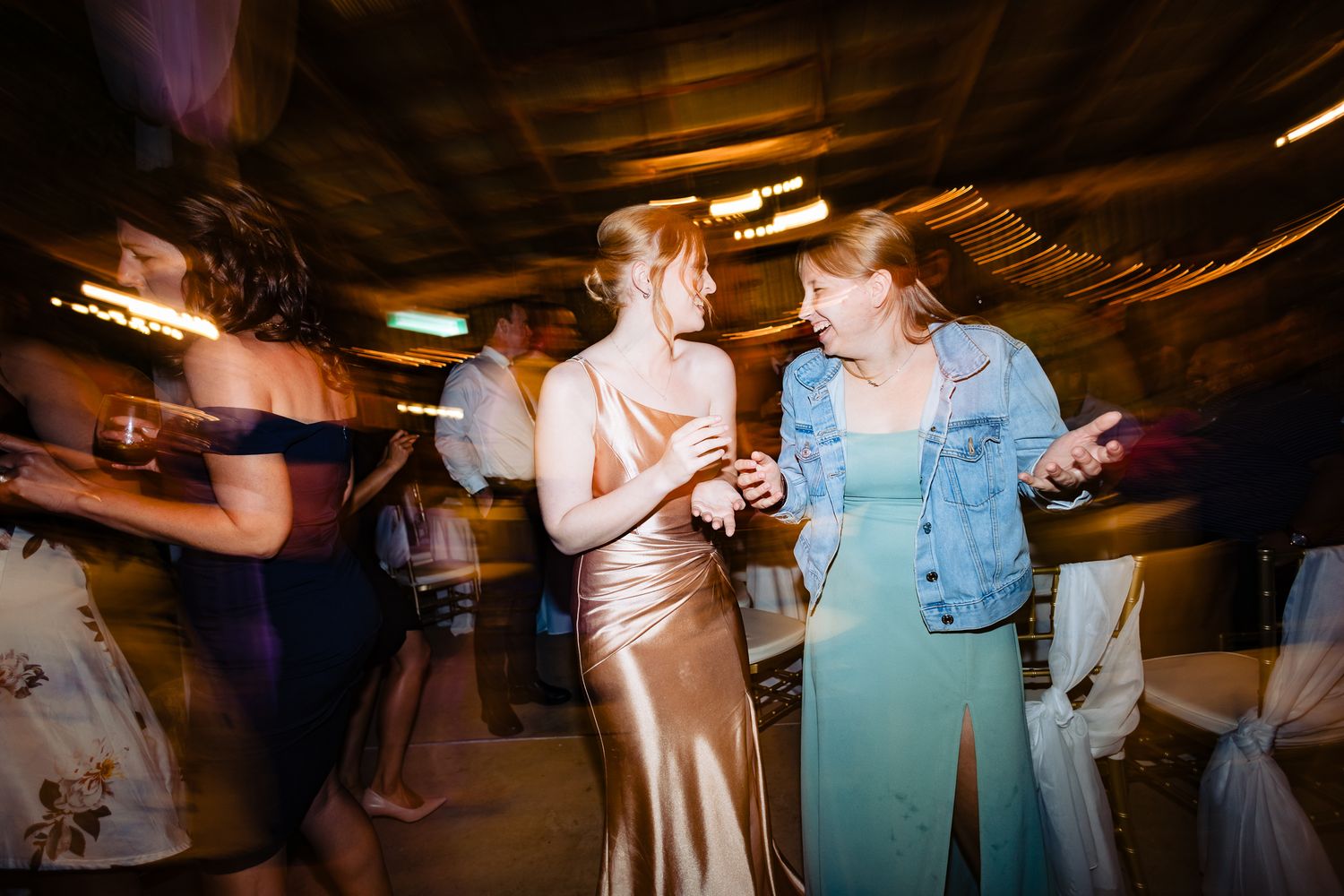 Wedding reception attendees dancing in a dimly lit venue with motion blur effects.