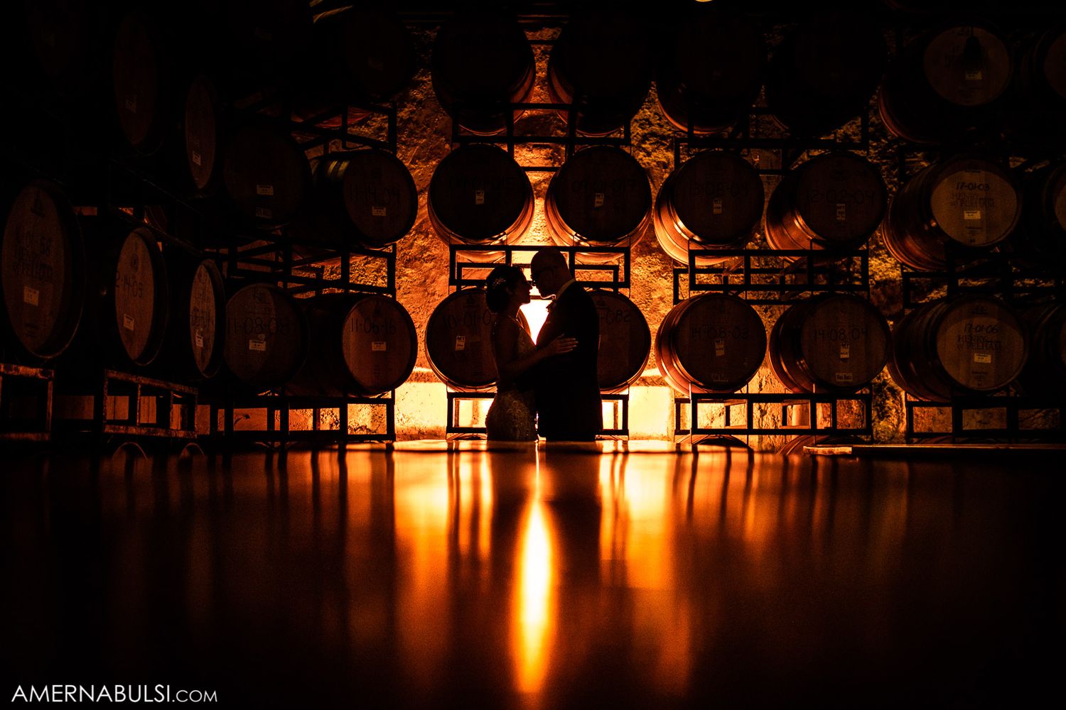 Silhouetted wine glasses create dramatic lighting effect against dark background.