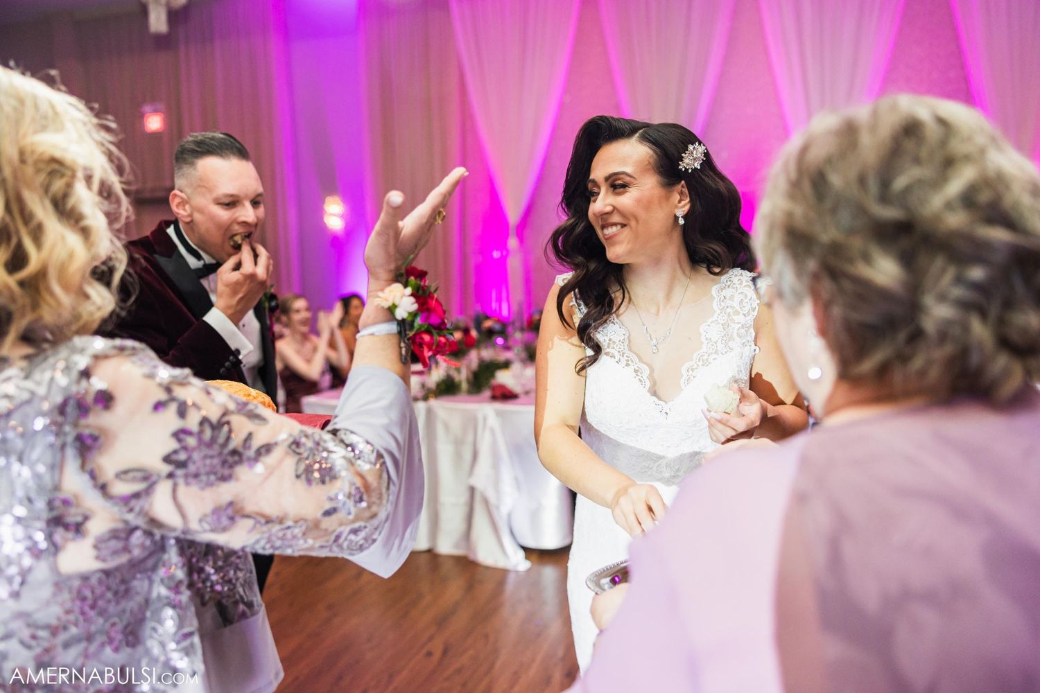 Celebration on a wedding dance floor with pink uplighting and white drapes in the background.