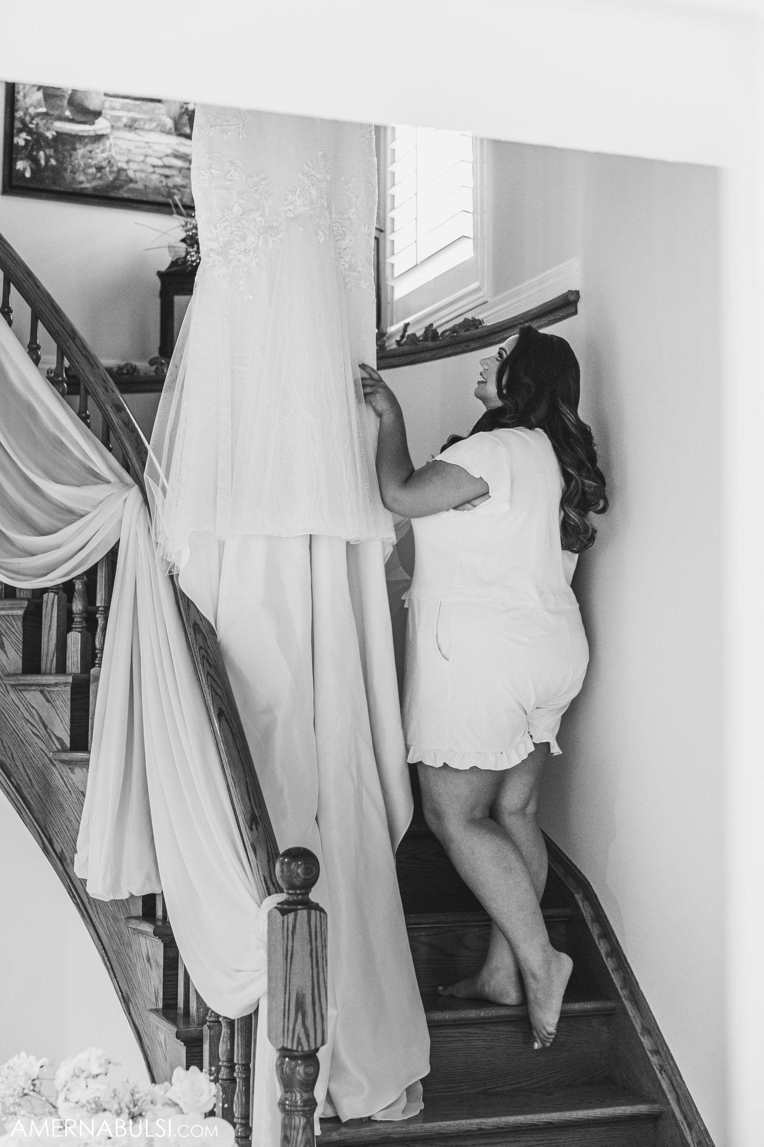 Black and white image of a wedding dress being carried up a staircase.