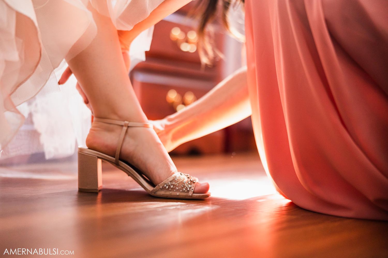 Close-up of feet showing beige block heel sandals against coral fabric and white tulle on hardwood floor.