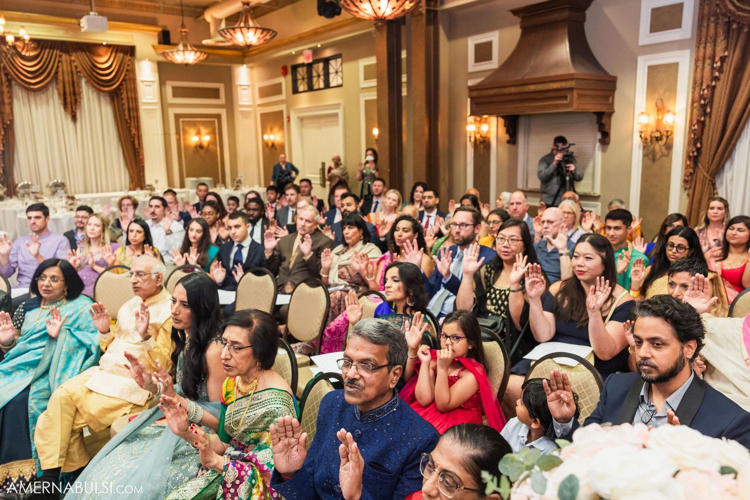 Guests celebrate at an elegant Indian wedding ceremony in a grand ballroom with ornate decor and lighting.