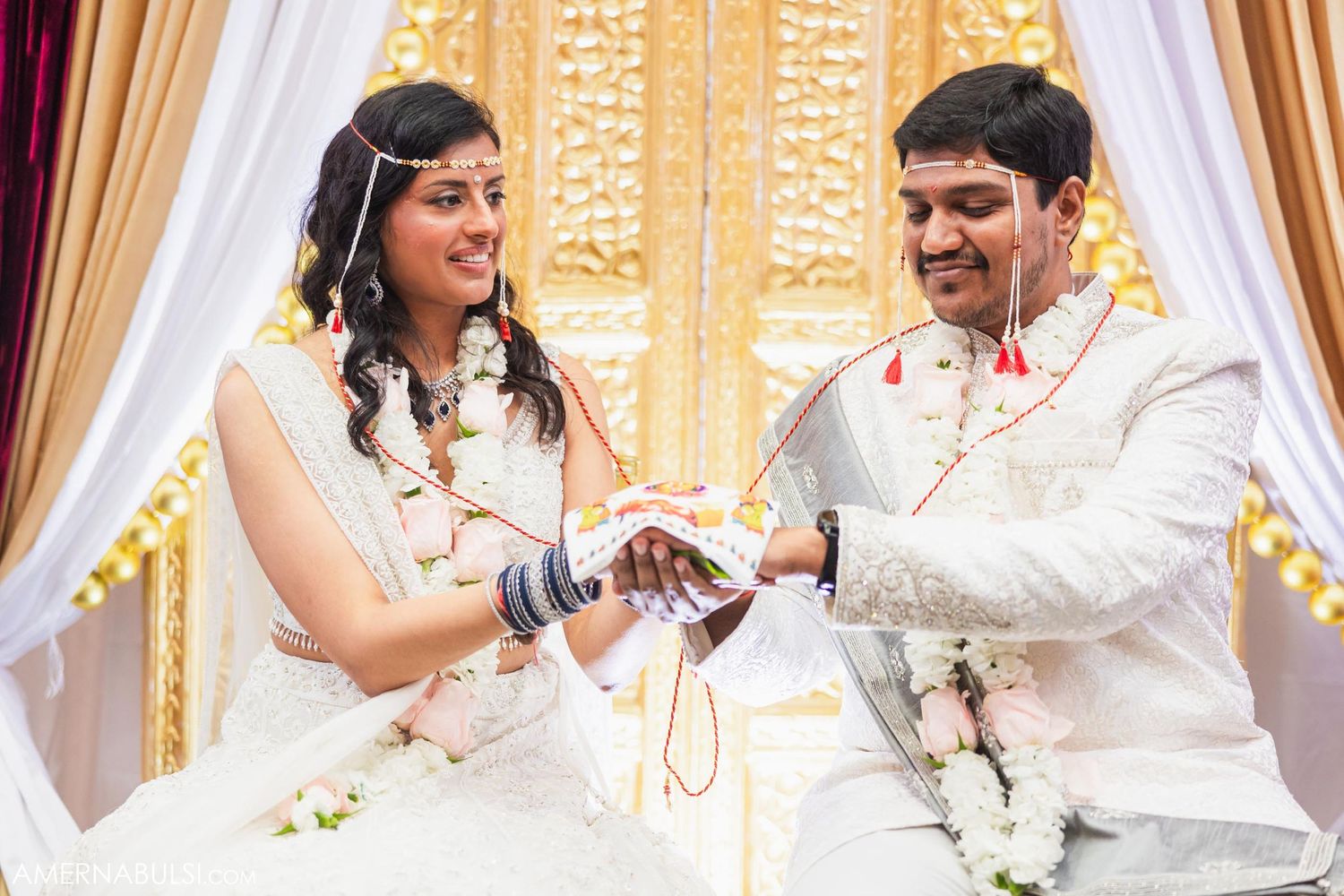 A traditional wedding ceremony with couple exchanging rings under decorative white and gold drapery.