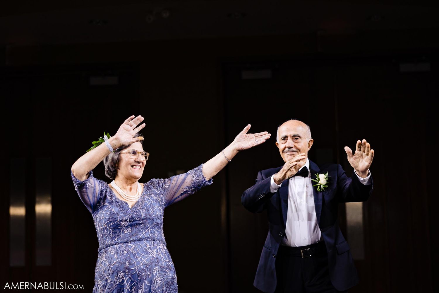 Dynamic shot of couple in formal attire gesturing enthusiastically in dark venue.