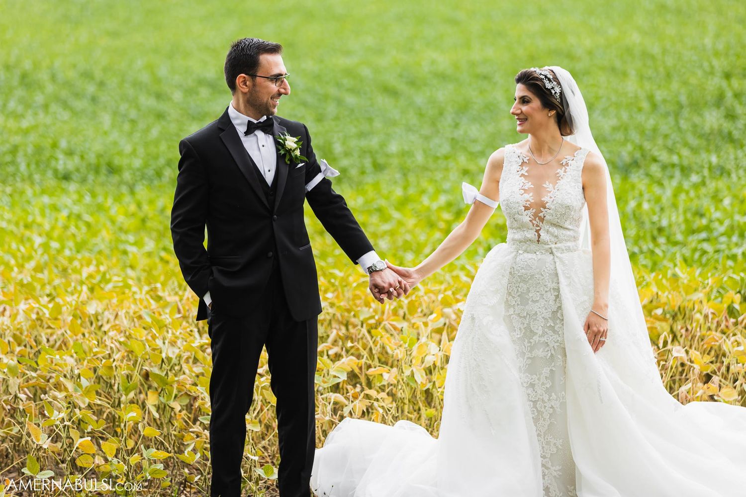 Joyful wedding couple holding hands in sunny meadow filled with yellow flowers.