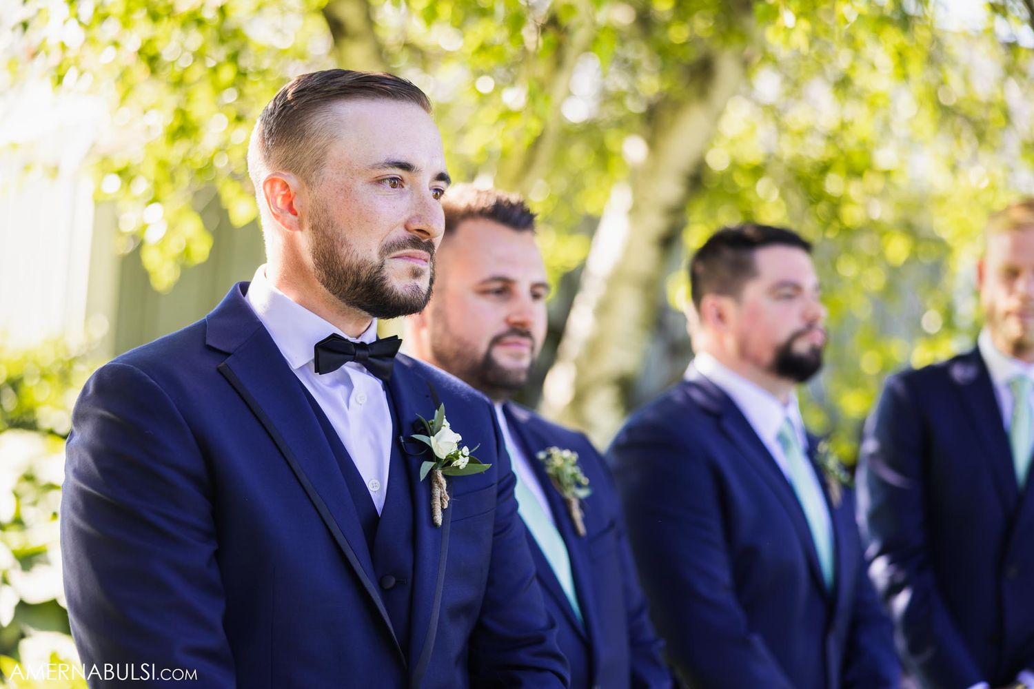 Groomsmen in navy suits standing during an elegant outdoor wedding ceremony.