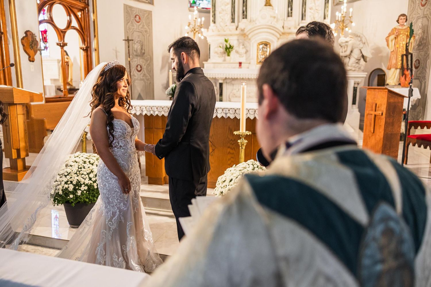 A wedding ceremony takes place in an ornate Catholic church with decorative altar and floral arrangements.