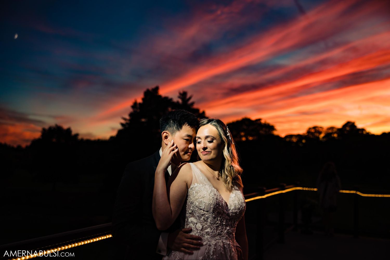 A dramatic sunset creates a romantic backdrop for an evening wedding portrait.