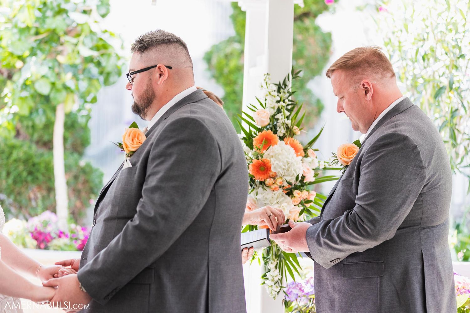 Two groomsmen in gray suits with orange boutonnieres standing at outdoor wedding altar.