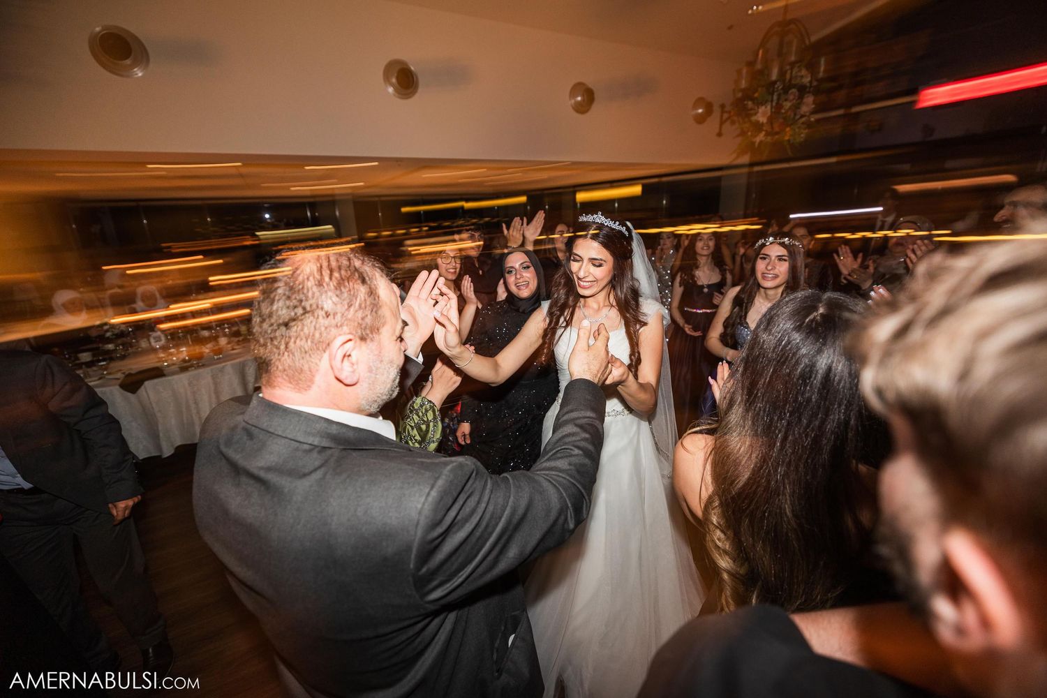 Guests dancing and celebrating at a lively indoor wedding reception with dramatic lighting.