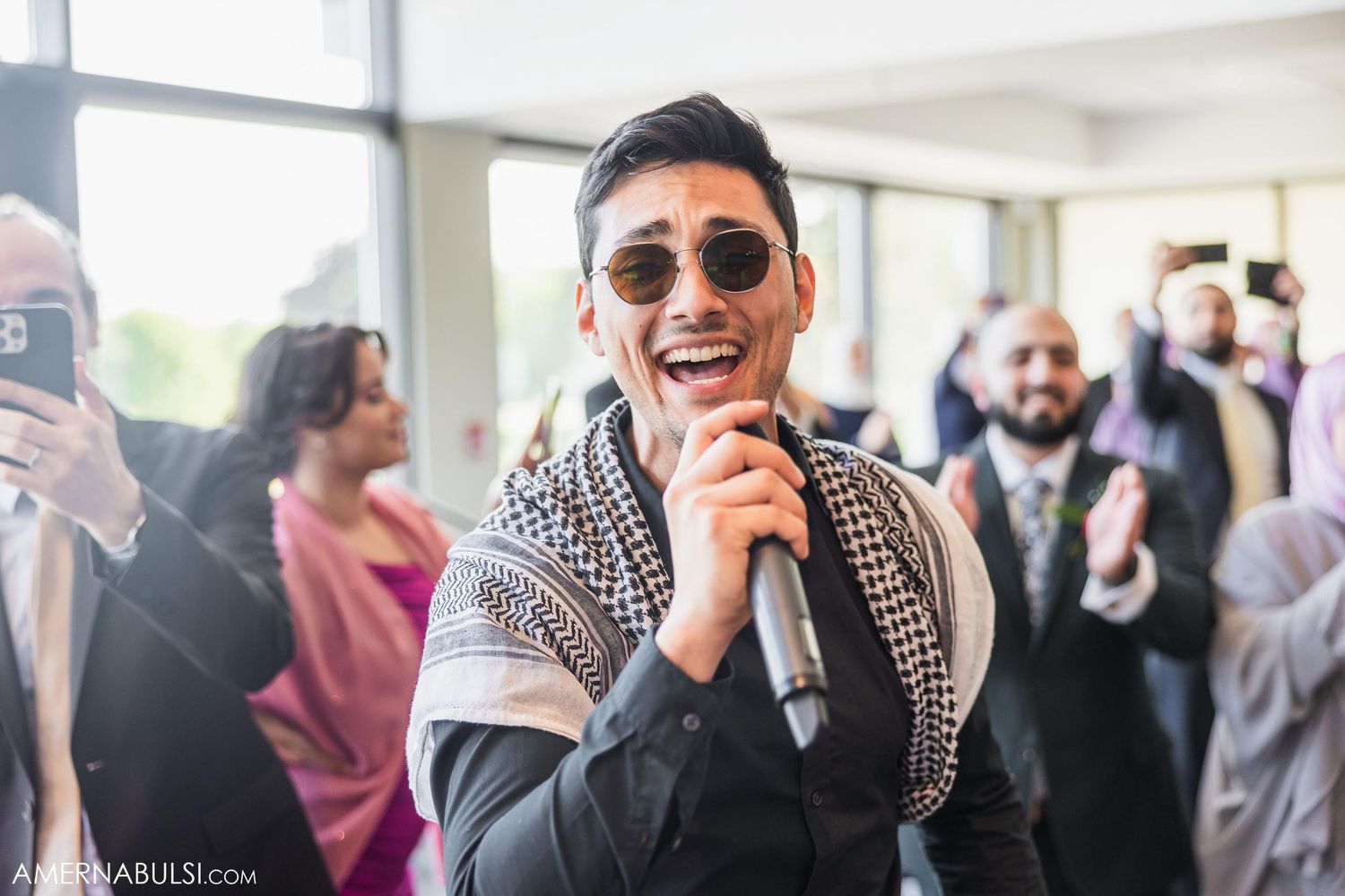 Singer performs with microphone wearing sunglasses and patterned scarf at wedding reception.