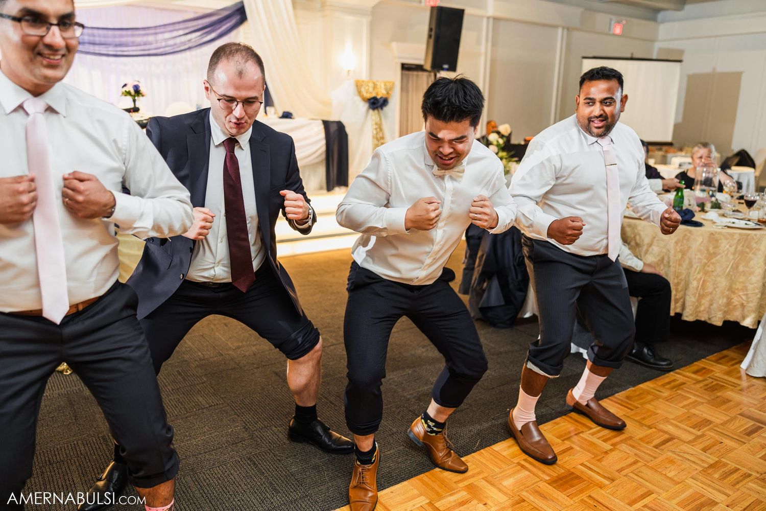 Guests showing off synchronized dance moves on a wooden dance floor at a wedding reception.