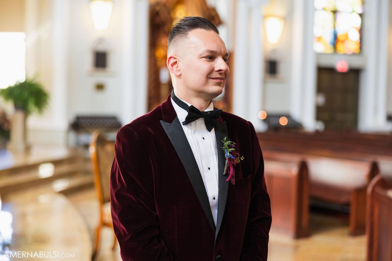 Wedding attire featuring burgundy velvet tuxedo with black bow tie in church setting.